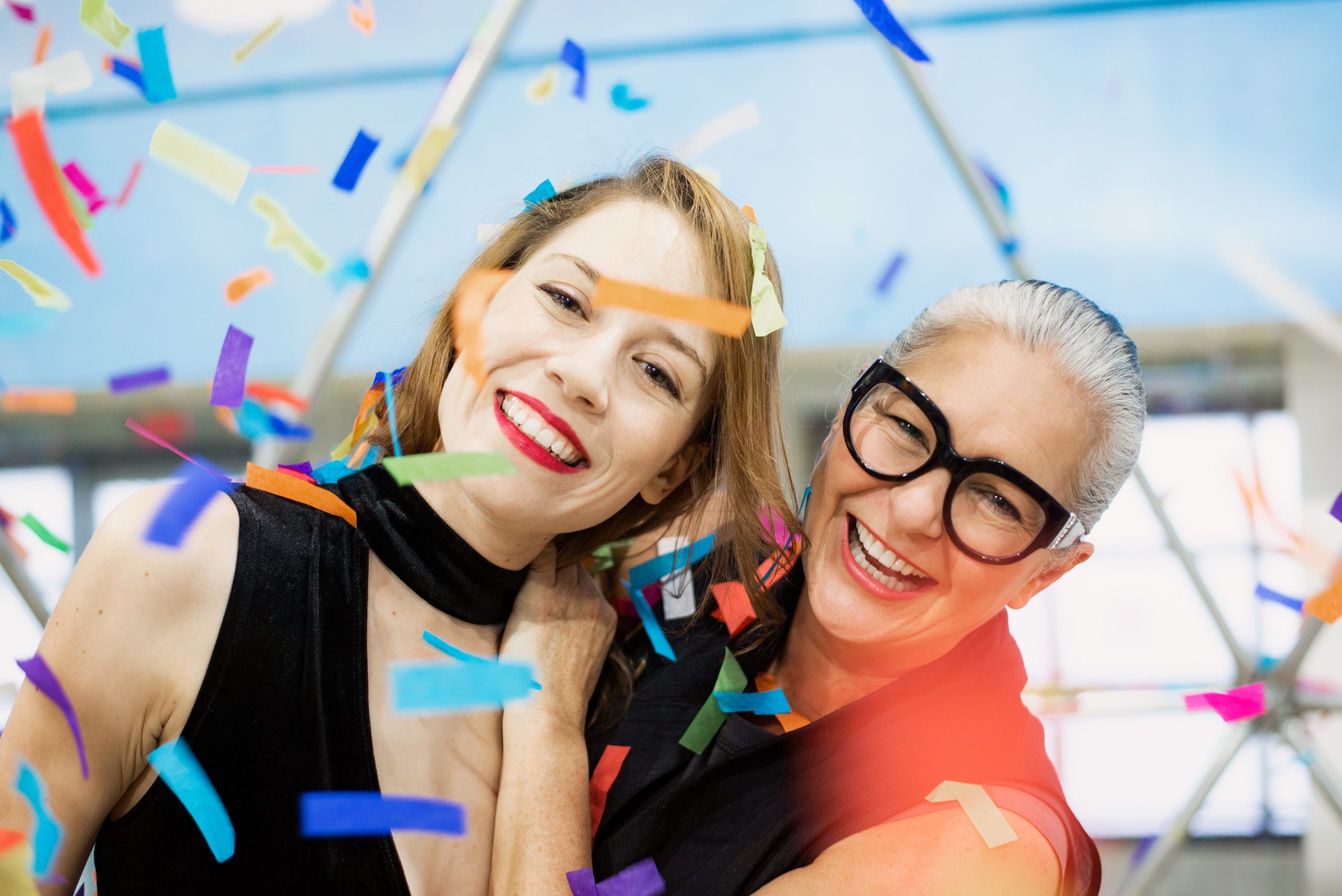 two-women-smiling-in-a-blizzard-of-rainbow-paper-confetti